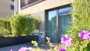 An outdoor seating area with a table and chairs, surrounded by lush greenery and flowers. - VARIAS Business Apartments (Elsau)
