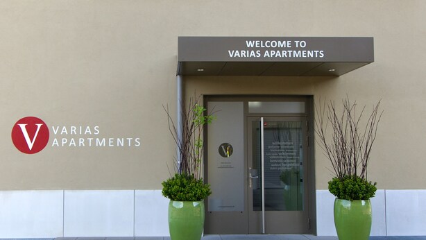 A building entrance with a sign reading "Welcome to Varias Apartments" and a logo with a red 'V'. - VARIAS Business Apartments (Elsau)