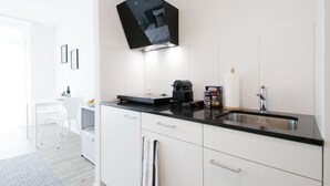 A modern kitchen with white cabinets, a black countertop, a coffee machine, and a hanging TV. - VARIAS Business Apartments (Elsau)