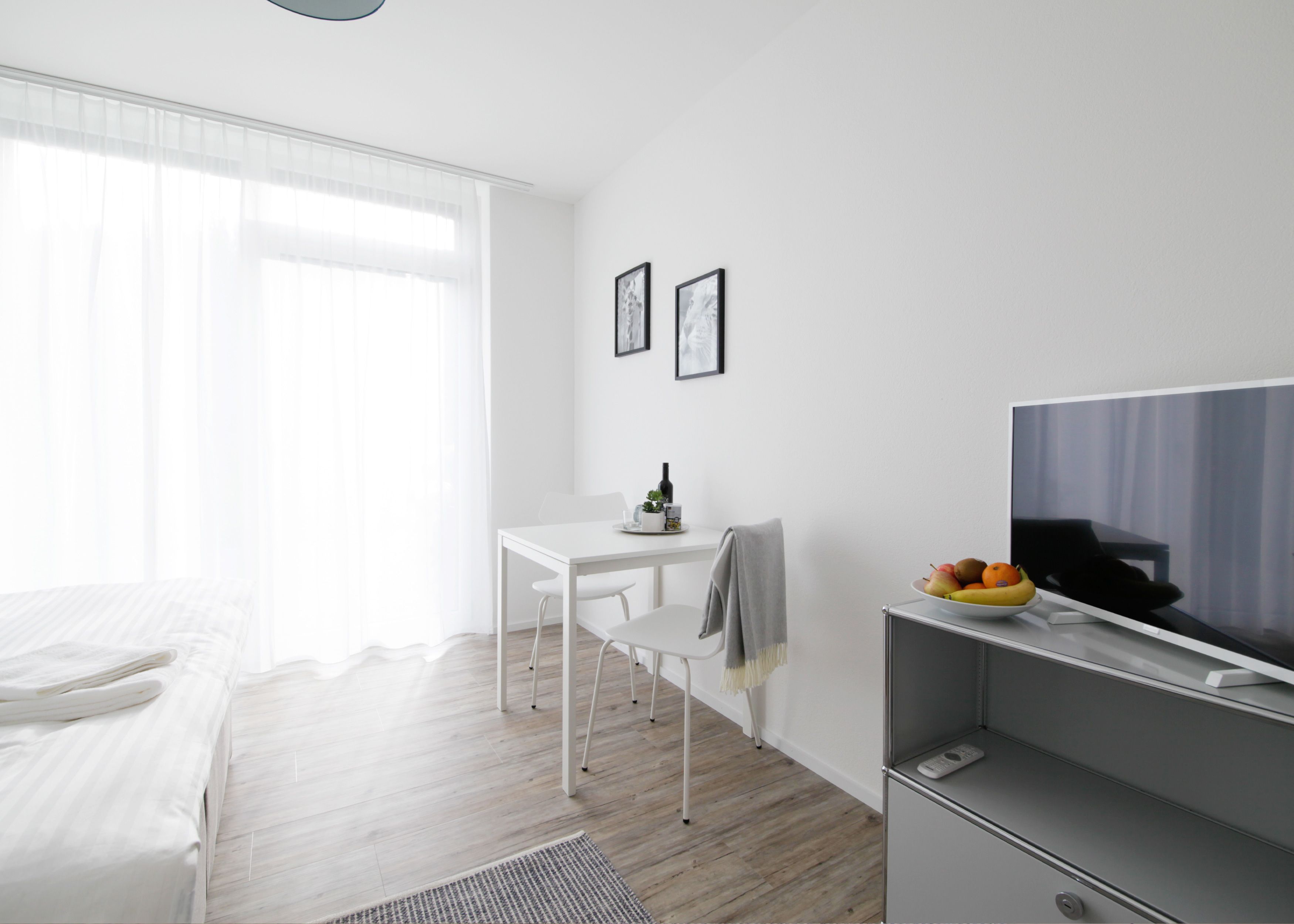 Une chambre d’hôtel moderne équipée d’un lit, d’un bureau, d’une chaise, d’une télévision et d’une petite table sur laquelle se trouve un saladier rempli de fruits.