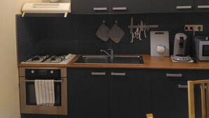 Una cocina compacta con armarios oscuros, estufa a gas, lavamanos y microondas.