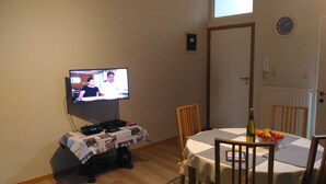 Un comedor con una mesa lista para dos personas, un televisor montado en la pared y una puerta al fondo.