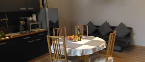 A small dining area with a round table, four chairs, and a bowl of fruit and a bottle of wine. There is a kitchen area with a microwave and a coffee maker.