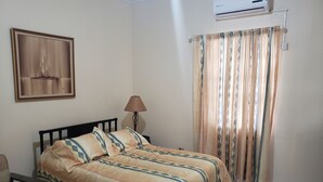 A bedroom with a bed, a lamp, an air conditioner, and a curtain. - The Barbican Haven (Kingston)