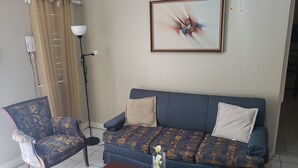A living room with a patterned sofa, a patterned armchair, a small table with a vase, a floor lamp, and a painting on the wall. - The Barbican Haven (Kingston)