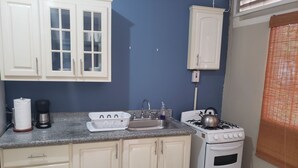 A compact kitchen with a gas stove, sink, and white cabinets. - The Barbican Haven (Kingston)