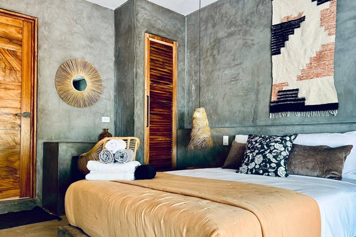 A bedroom with a large bed, a wooden wardrobe, a round mirror, and a hanging light fixture.