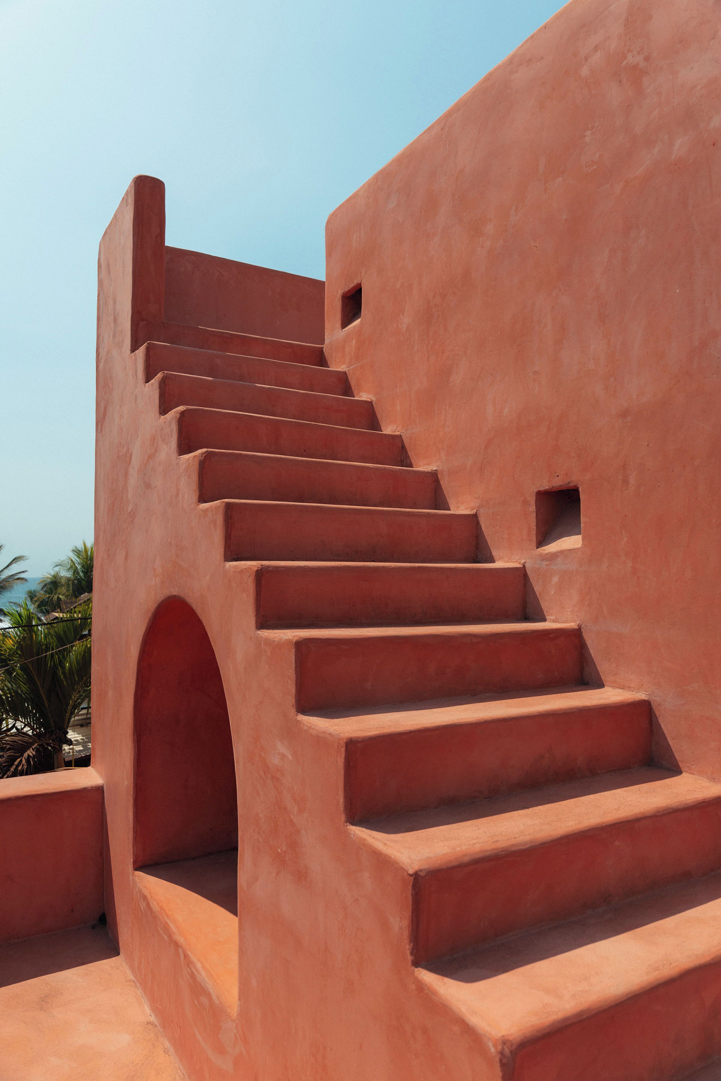 Unos escalones de color terracota conducen a un balcón con vista despejada a palmeras y al cielo.
