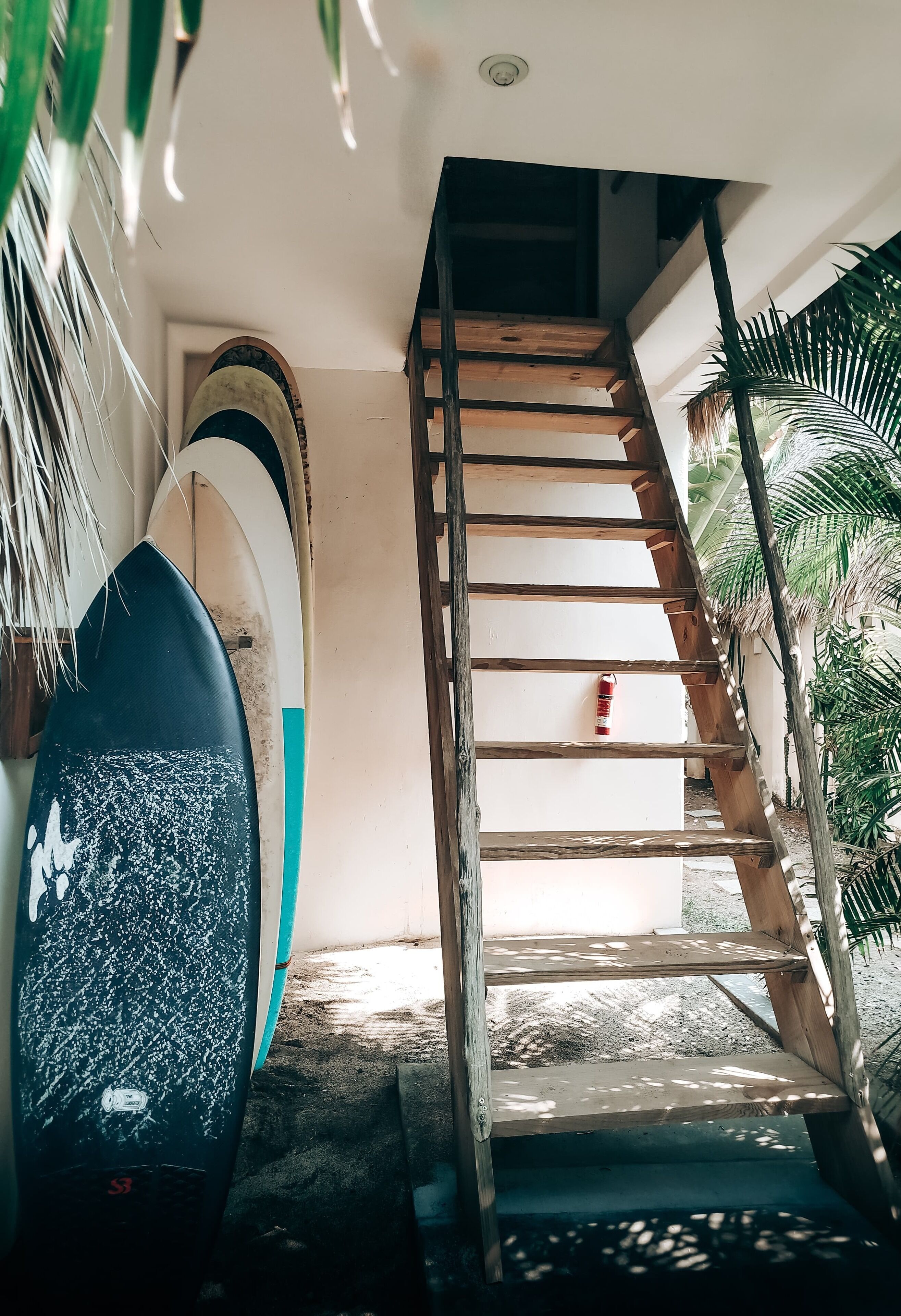 A wooden staircase leading to a room with surfboards leaning against the wall.