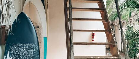 A wooden staircase leading to a room with surfboards leaning against the wall.