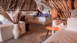A room with a thatched roof, a bed with a canopy, a small table, and a sofa.