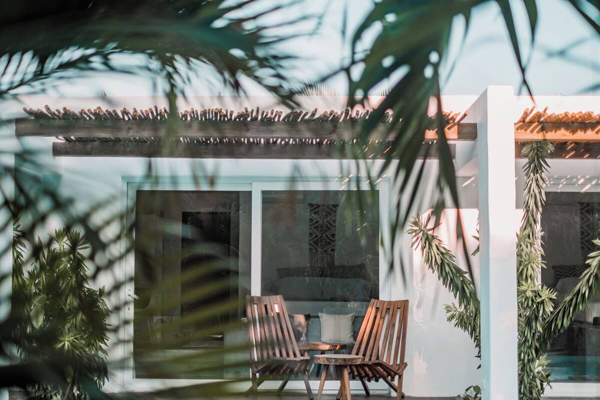 A modern house with a glass facade, a wooden deck, and a dining area with two chairs.