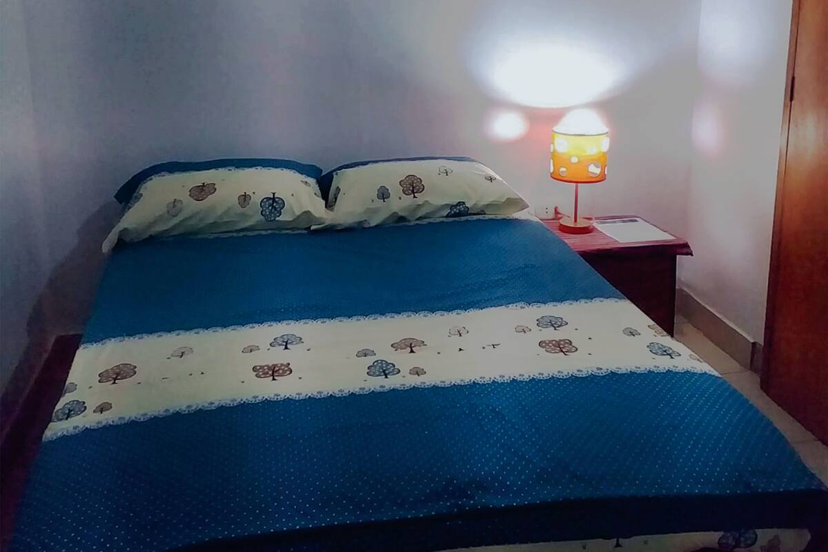 A bedroom with a bed, a nightstand, a lamp, and a painting on the wall.