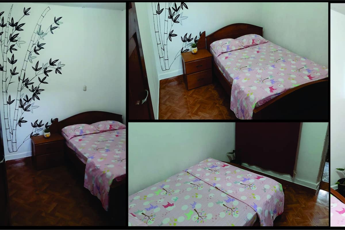 A bedroom with two beds, a wooden floor, a wall with a bamboo plant mural, a red curtain, and a small potted plant.