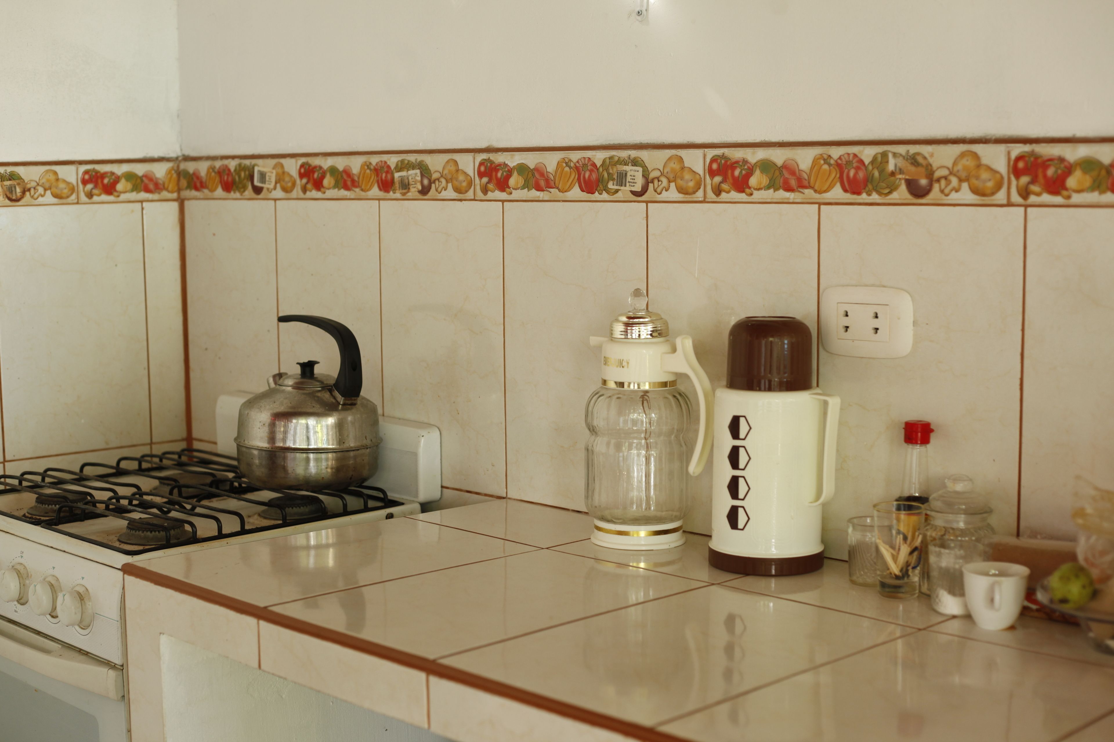 A kitchen with a stove, a kettle, a coffee maker, and various kitchen items on the counter.