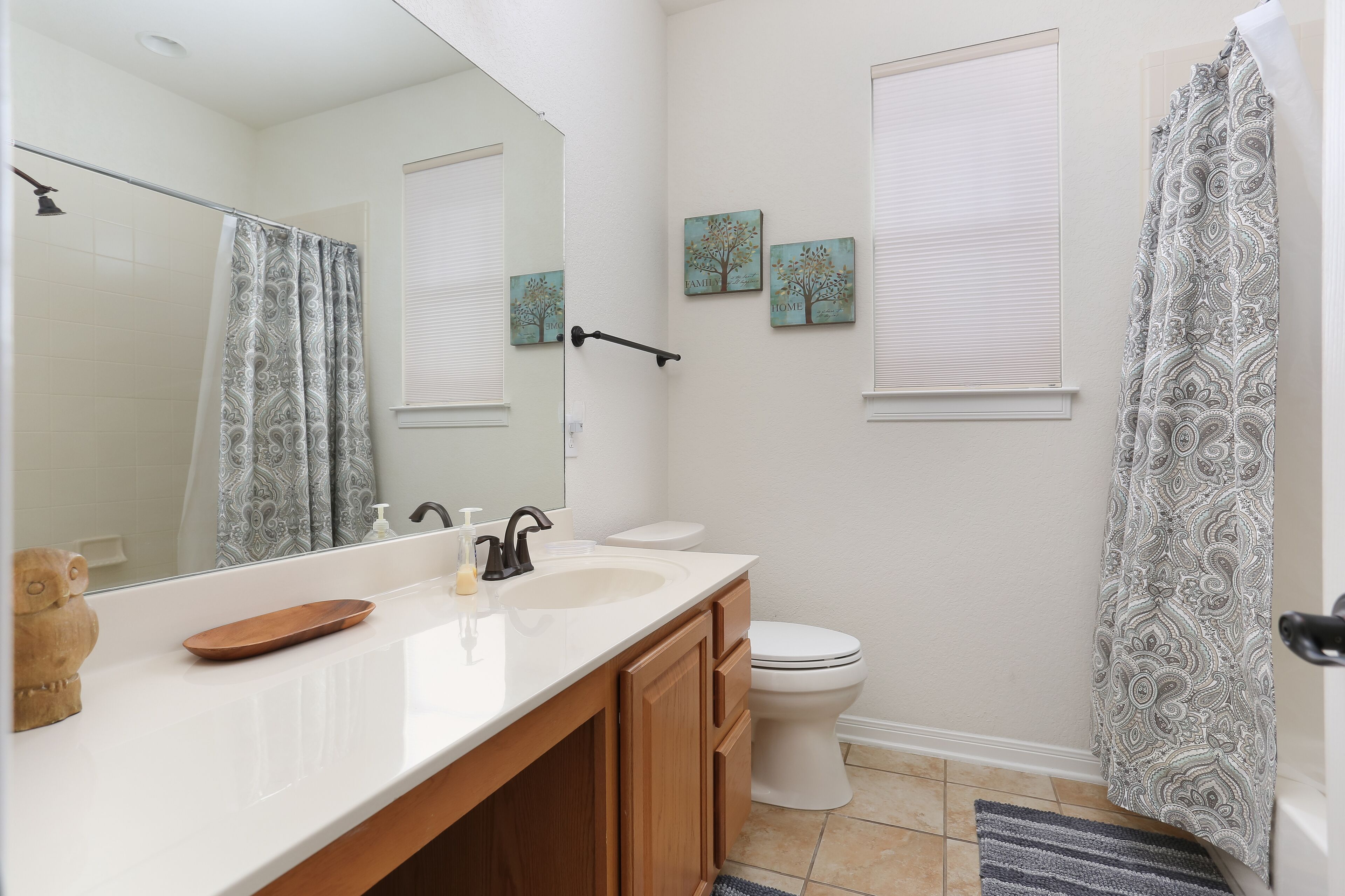 A bathroom with a white sink, wooden cabinets, a mirror, a toilet, and a shower curtain.