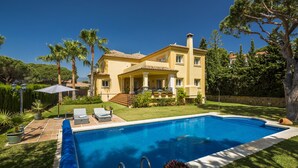 Une grande maison avec une piscine, un patio couvert et un jardin bien entretenu.