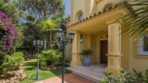 Un jardin bien entretenu avec un patio qui mène à un bâtiment jaune dont l’entrée est ornée de carreaux.