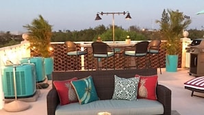 Eine Dachterrasse mit einer Sofagruppe, zwei Stühlen, einem Tisch und einem Grill.