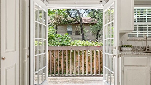 A view through an open door to a wooden deck with a fence, leading to a house with a red roof. - Circle Town hm near the golf course (Austin)