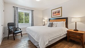 A neatly arranged bedroom with a large bed, a chair, a bedside table with a lamp, and a window with curtains. - Circle Town hm near the golf course (Austin)