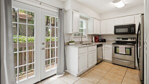 A kitchen with white cabinets, a stainless steel refrigerator, a microwave, an oven, and a sink. - Circle Town hm near the golf course (Austin)