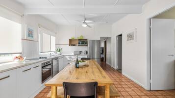 A modern kitchen with white cabinetry, a wooden dining table, and a ceiling fan.
