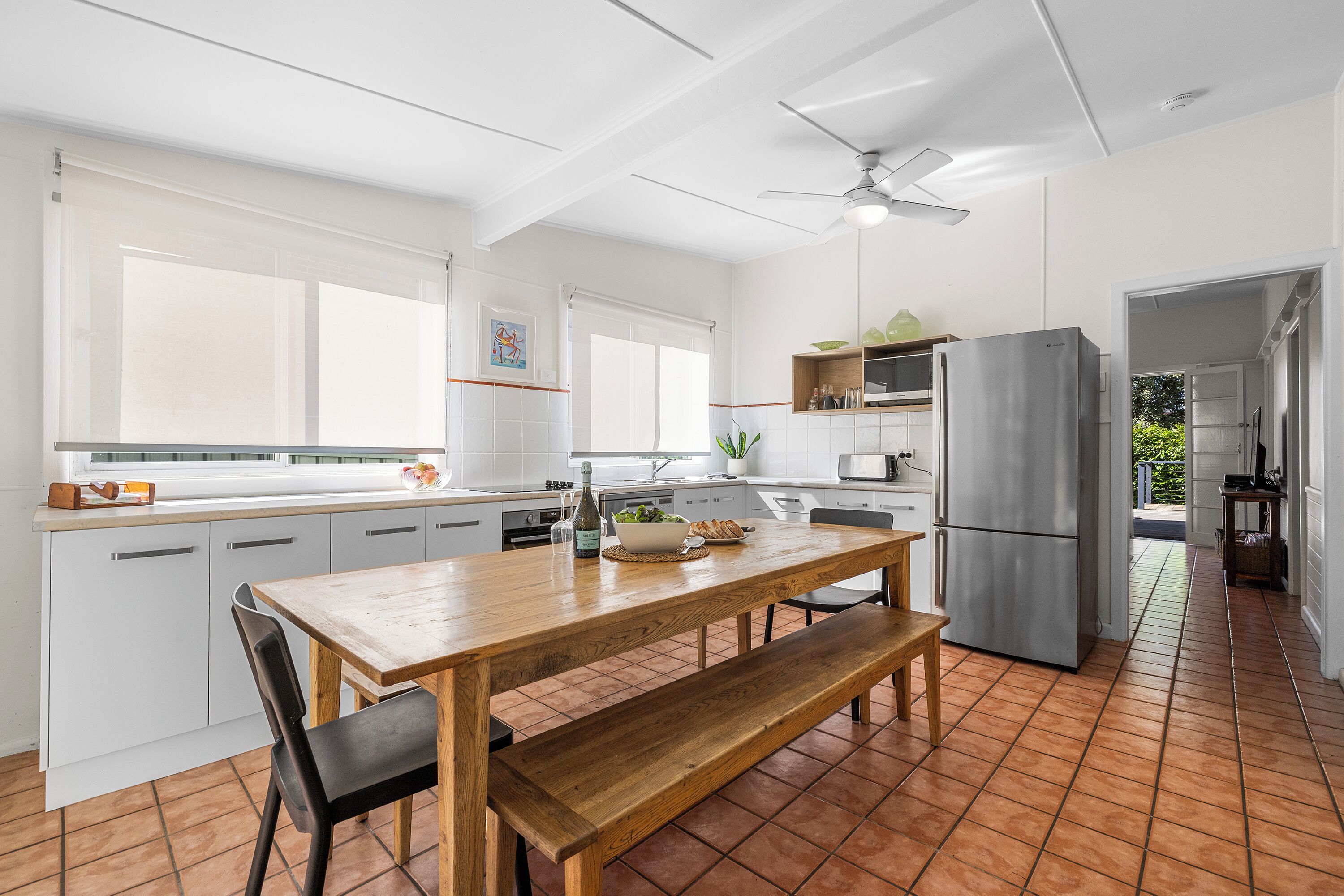 A modern kitchen with white cabinetry, a wooden dining table, and a built-in oven.