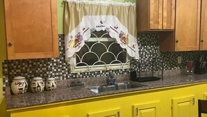 A kitchen with yellow cabinets, a sink, and a window with a decorative curtain.