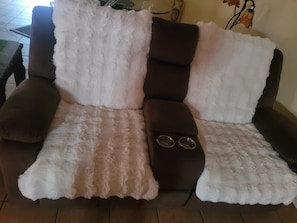 Ein Sofa mit flauschigem, weiß-braunem Stoff, ein Beistelltisch mit zwei Getränkehaltern und ein kleines dekoratives Element an der Wand.