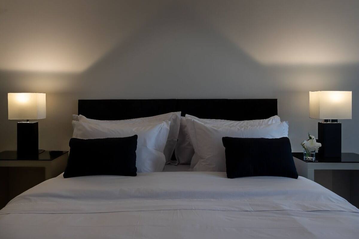 A neatly made bed with white linens and black pillows, flanked by two bedside tables with lamps.