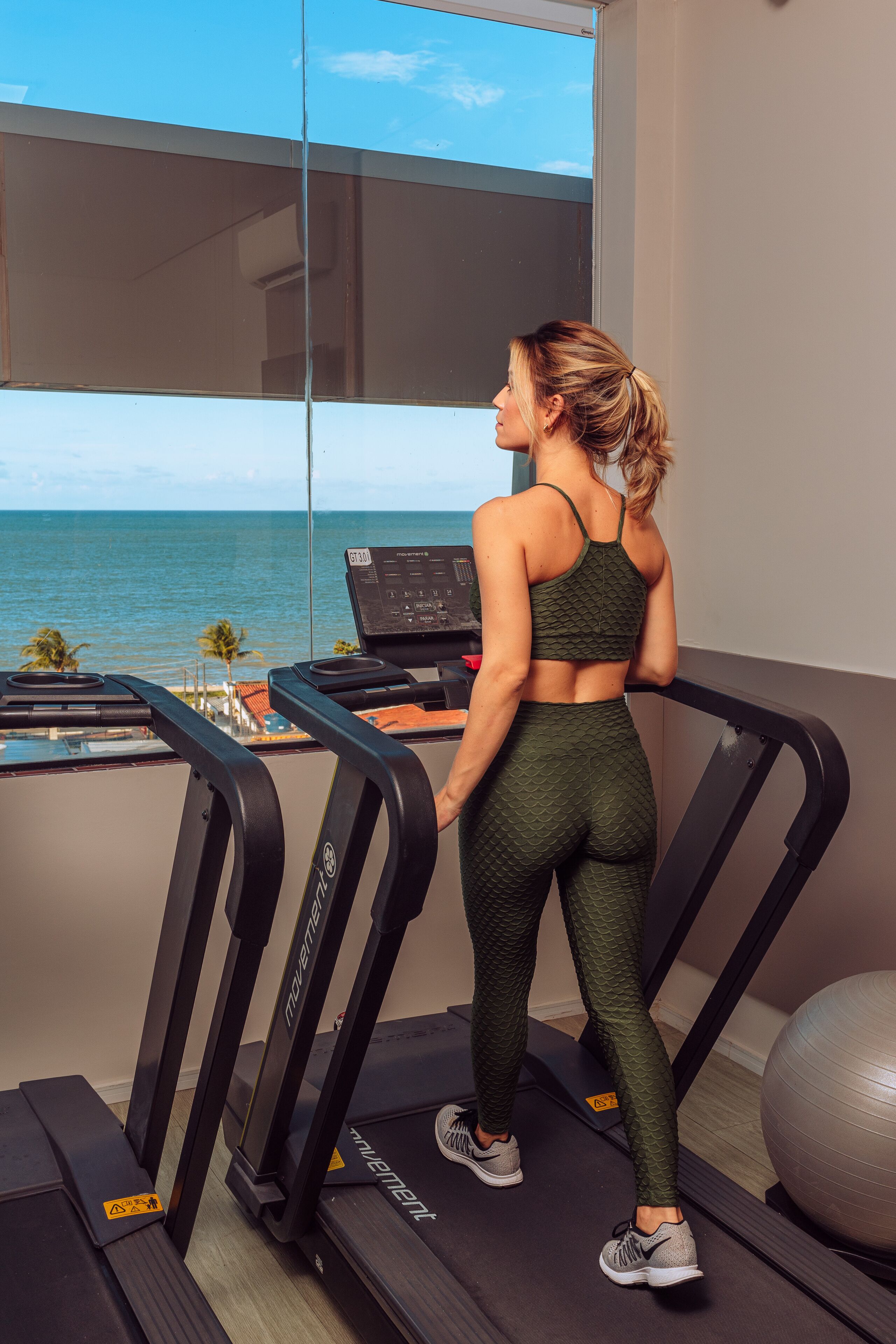 A woman on a treadmill with a view of the ocean through large windows.