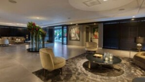 A spacious lobby with a modern design, featuring a seating area with sofas and armchairs, a coffee table, and a large vase with flowers. - LS Hotel (João Pessoa)