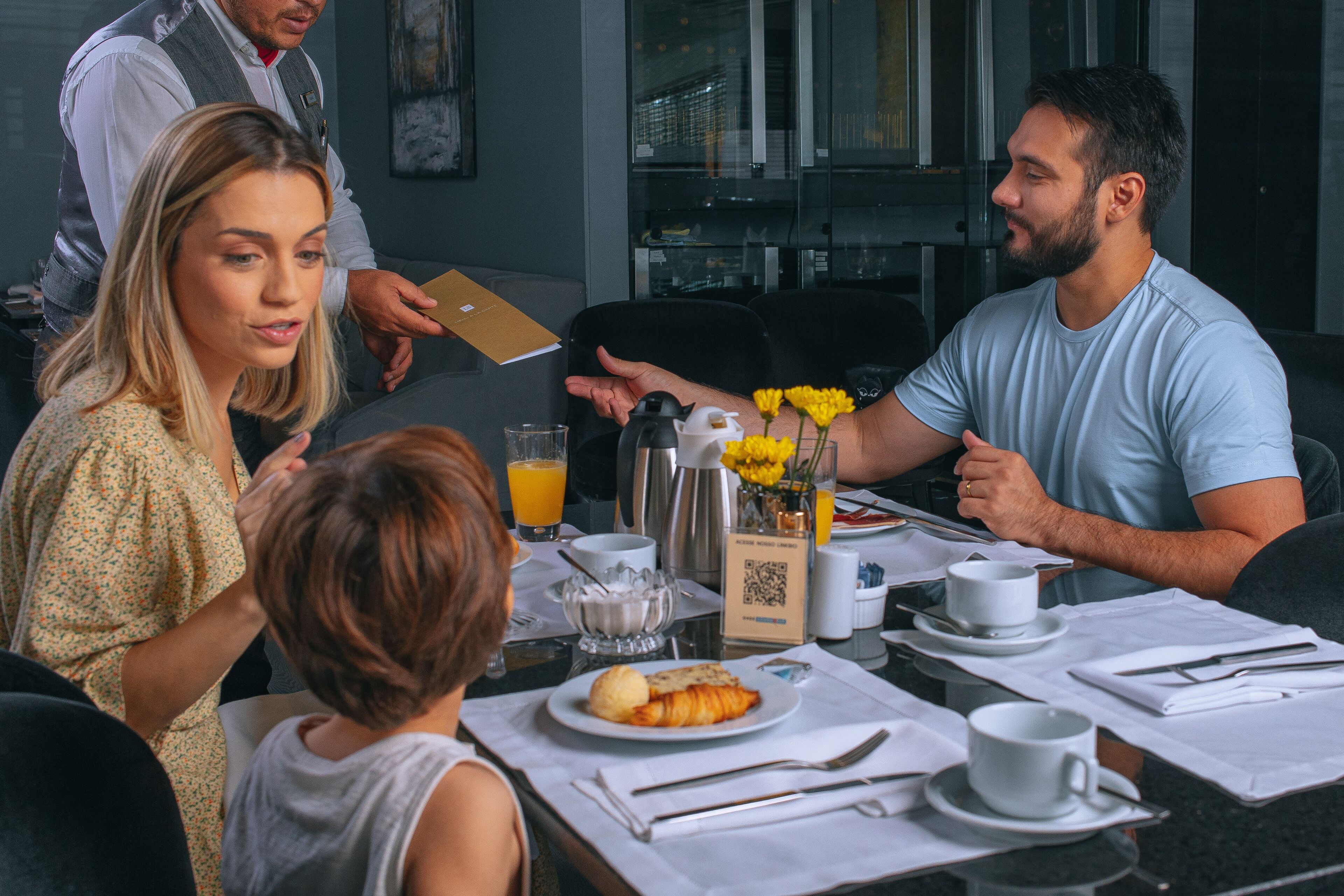 Desayuno preparado para cuatro personas, con platos de comida, tazas y una cafetera.