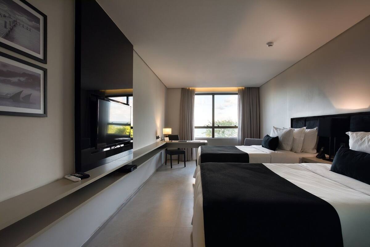 A modern hotel room with two beds, a flat-screen TV, a desk, and a window with curtains.