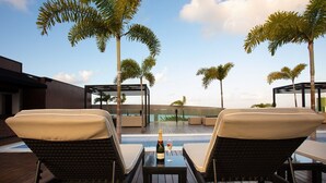 A rooftop pool area with lounge chairs, a table with a bottle of champagne, and a glass of champagne. - LS Hotel (João Pessoa)