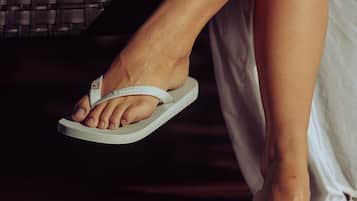 A close-up of a person's feet wearing white flip-flops, standing on a wooden floor.