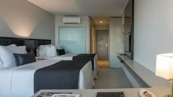 A hotel room with two beds, a TV, a desk with a lamp, and a magazine on the table.
