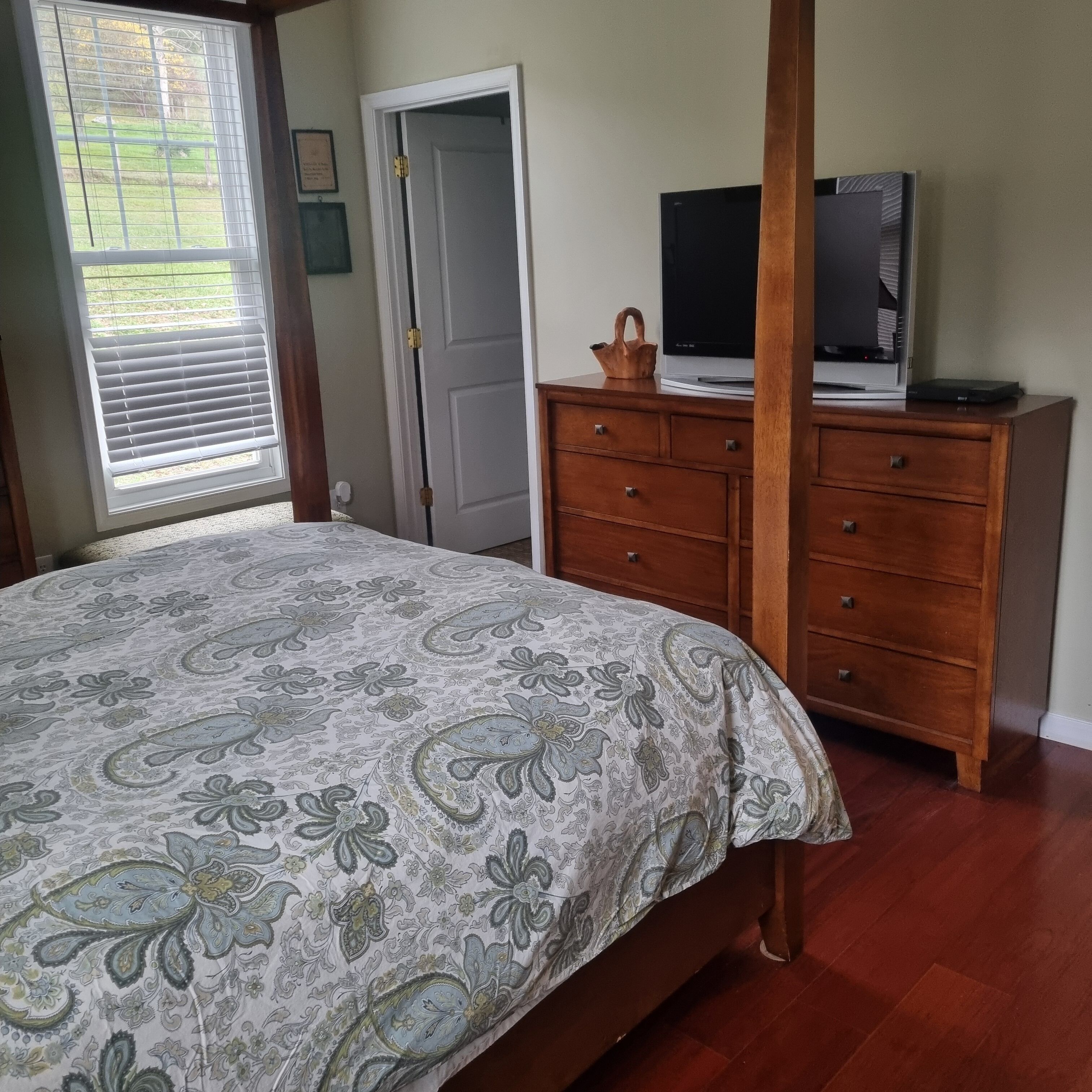A bedroom with a large bed, wooden dresser, and a television on a stand.