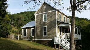 A two-story house with a porch and a staircase leading to the second floor. - Lost River WV-Relaxing 3br/2bath farmhouse-dog friendly-  treetop deck-workspace (Mathias)