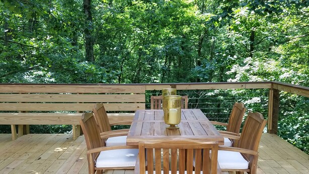 A wooden deck with a table and chairs, surrounded by lush greenery. - Lost River WV-Relaxing 3br/2bath farmhouse-dog friendly-  treetop deck-workspace (Mathias)