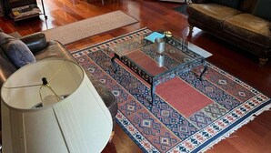 A living room with a sofa, a coffee table, a lamp, a rug, and a dining area with chairs and a table. - Lost River WV-Relaxing 3br/2bath farmhouse-dog friendly-  treetop deck-workspace (Mathias)