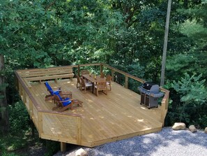 Une terrasse en bois avec un banc, des chaises et un barbecue.