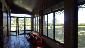 A covered hallway with a boat, large windows, and a view of people outside. - Pleasant beachfront house on Guaecá beach, São Sebastião, SP (São Sebastião)