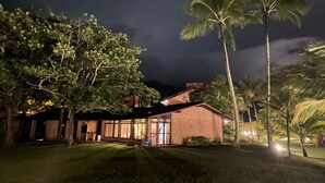 A well-lit building with a brick exterior, surrounded by lush greenery and palm trees. - Pleasant beachfront house on Guaecá beach, São Sebastião, SP (São Sebastião)