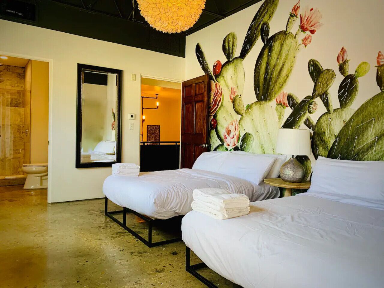 Hotelkamer met twee bedden, een grote cactusmuur, een spiegel en een badkamer met toilet en douche.