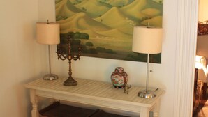 Una habitación con una consola, dos lámparas, un florero y un cuadro de colinas ondulantes.