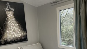 A bedroom with two single beds, a window with curtains, a painting on the wall, and a view of trees outside. - Lillibelles lake house (Ashford)