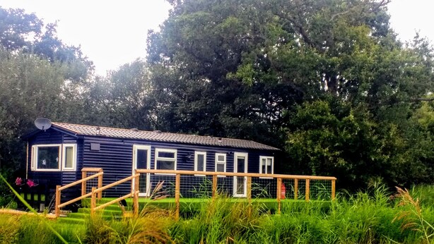 A house with a satellite dish, a fenced deck, and a pond in front. - Lillibelles lake house (Ashford)
