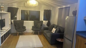 A compact living space with a sofa, two armchairs, a small rug, a TV, and a refrigerator. - Lillibelles lake house (Ashford)